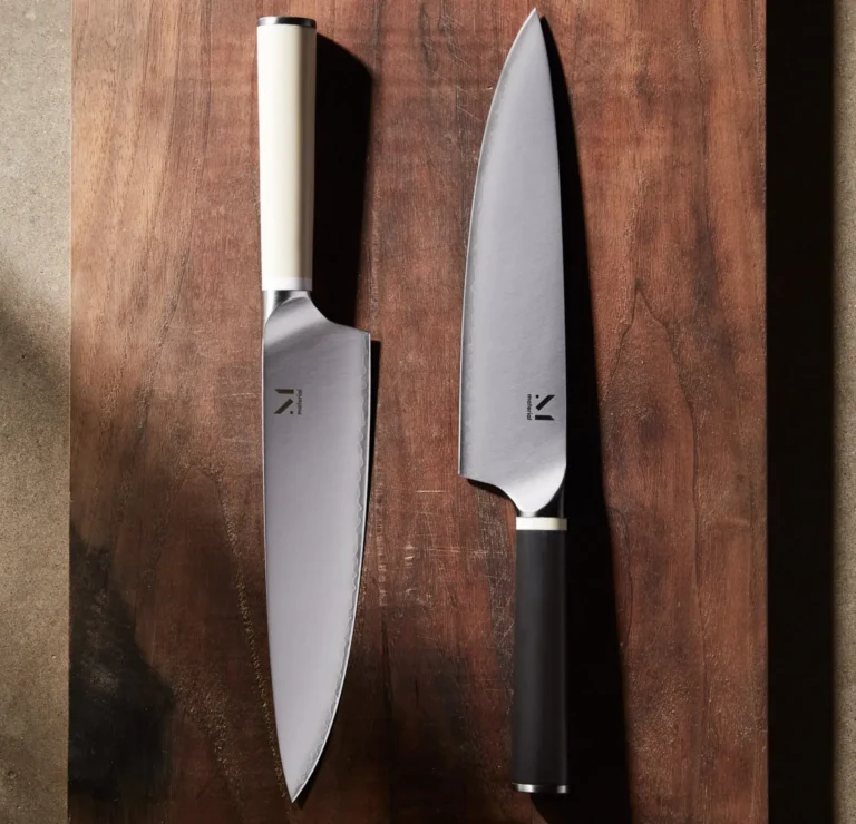 Two chef knives with distinct handles, one white and one black, placed parallel on a wooden cutting board surface.