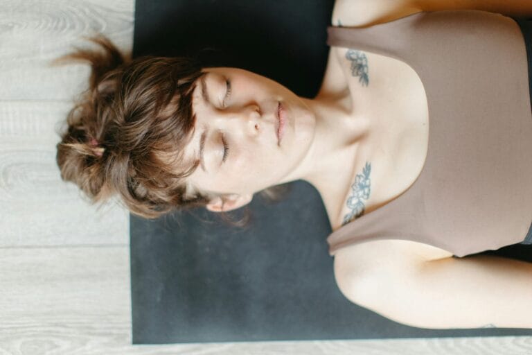 Close-up image of woman's face as she lies down on black yoga mat. Her eyes are closed.