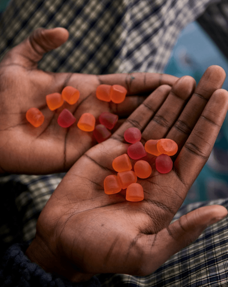 Two hands holding several small, orange and red gummy candies against a plaid fabric background.