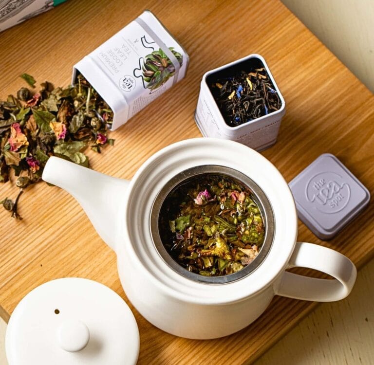 Loose leaf zero waste tea in a ceramic teapot alongside refillable metal tins, highlighting plastic free tea and sustainable tea packaging.