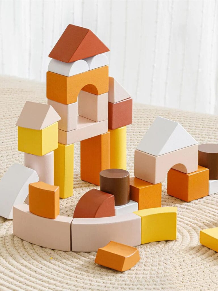 Colorful wooden blocks are stacked in various shapes and sizes on a beige surface, forming a tower with arches and pointed tops.