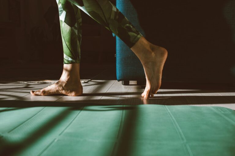 Close-up of woman's feet walking next to a green yoga mat.