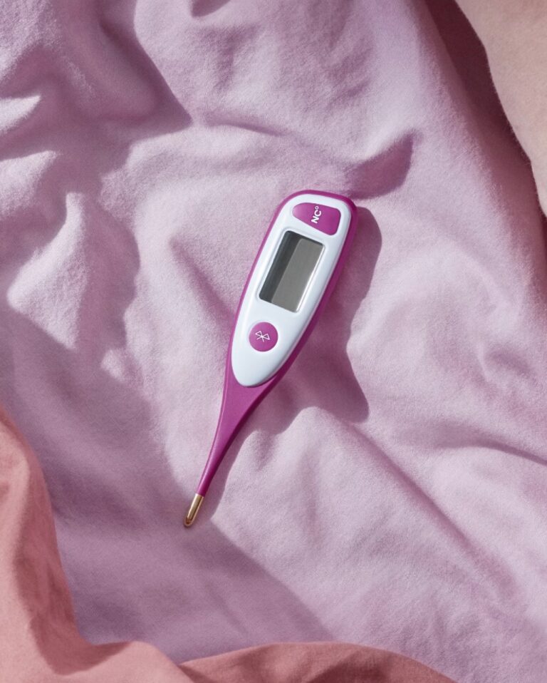 Digital thermometer with a pink and white design resting on a pink fabric surface.