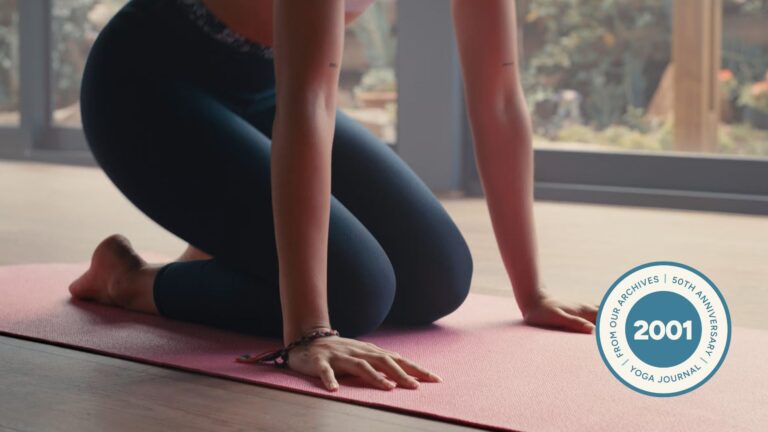 Woman kneeling on a yoga mat with her hands beneath her shoulders about to lift herself into Lolasana or Pendant Pose