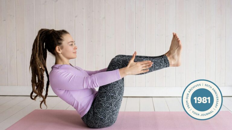Woman in pink shirt and gray leggings practicing Boat Pose (Navasana) on a pink yoga mat.