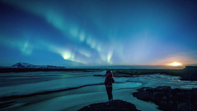 Woman standing beneath the northern lights on winter solstice contemlating weekly horoscope for December 21-27, 2025