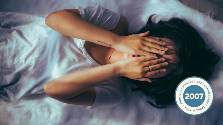 Woman lying on the floor practicing restorative yoga with her hands over her face