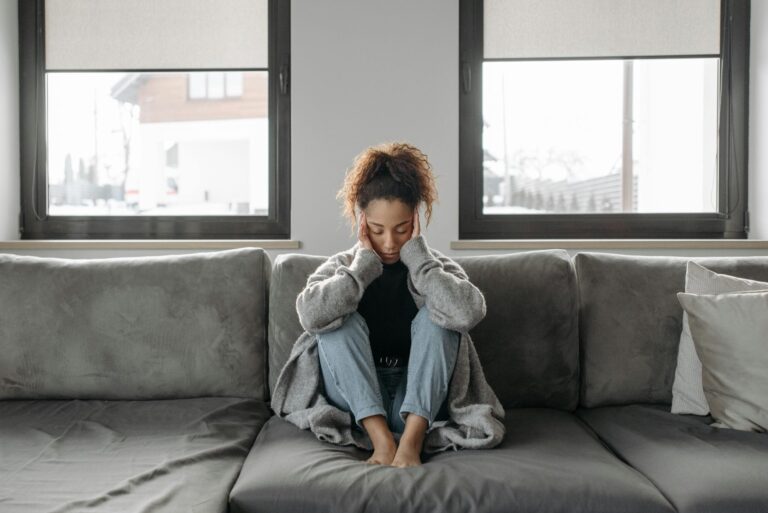 Woman sitting on couch with head in her hands.