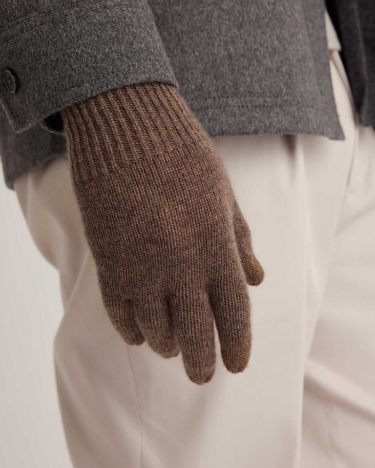 Close-up of a person wearing a gray coat, beige pants, and a brown wool glove.