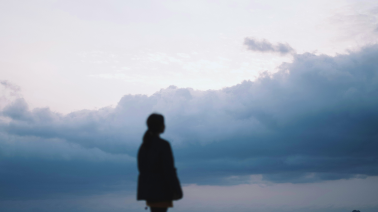 Woman staring off into a cloudy, overcast day during winter while contemplating the weekly horoscope for February 1-7, 2026
