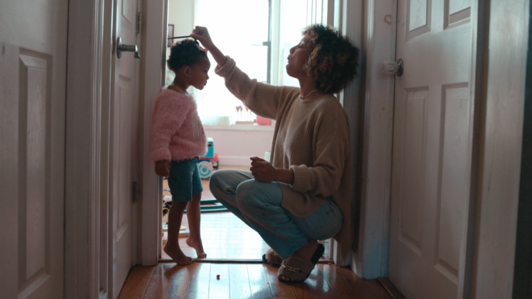 Mom measuring her toddler daughter during the childhood stage of life against a doorway