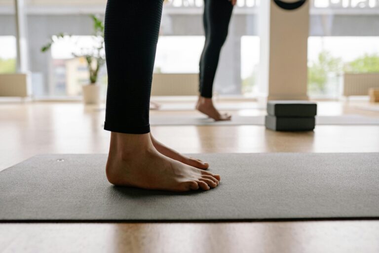 Close-up of people's feet standing on a black yoga mat.
