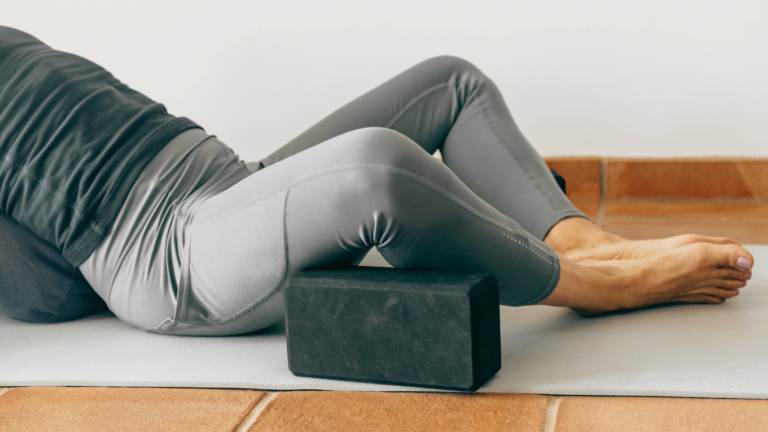 A person on a yoga mat using yoga props including a block and a bolster