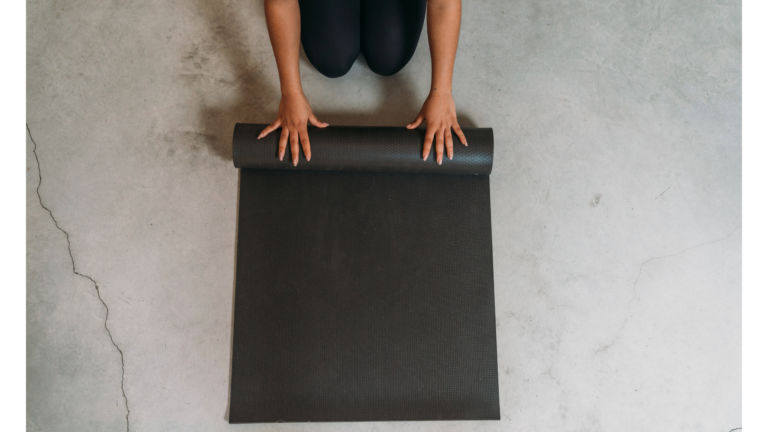 A woman crouching on the ground rolling up one of the best yoga mats