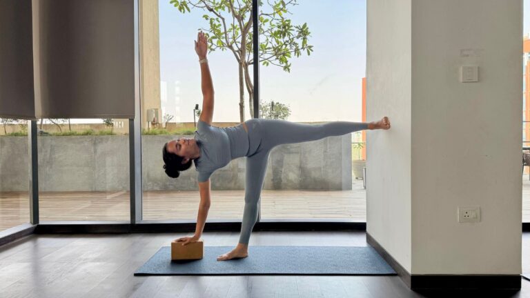 Yoga instructor Riya Davda practicing Half Moon Pose against a wall.