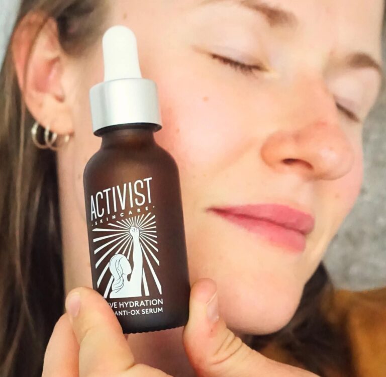 Sustainable Jungle's testing of Activist Skincare Active Hydration Vit C+ Anti-Ox Serum held against the face, showing the frosted glass dropper bottle with raised fist logo - Our guide to the best natural face serums
