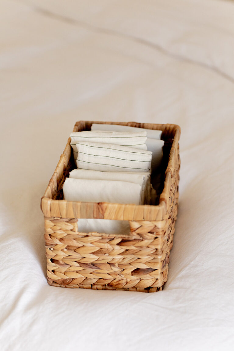 A woven basket filled with neatly folded white cloths sits on a white surface.