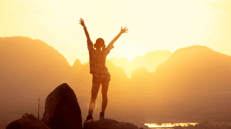 Woman hiker watching sunrise over the mountains with her arms thrown in the air