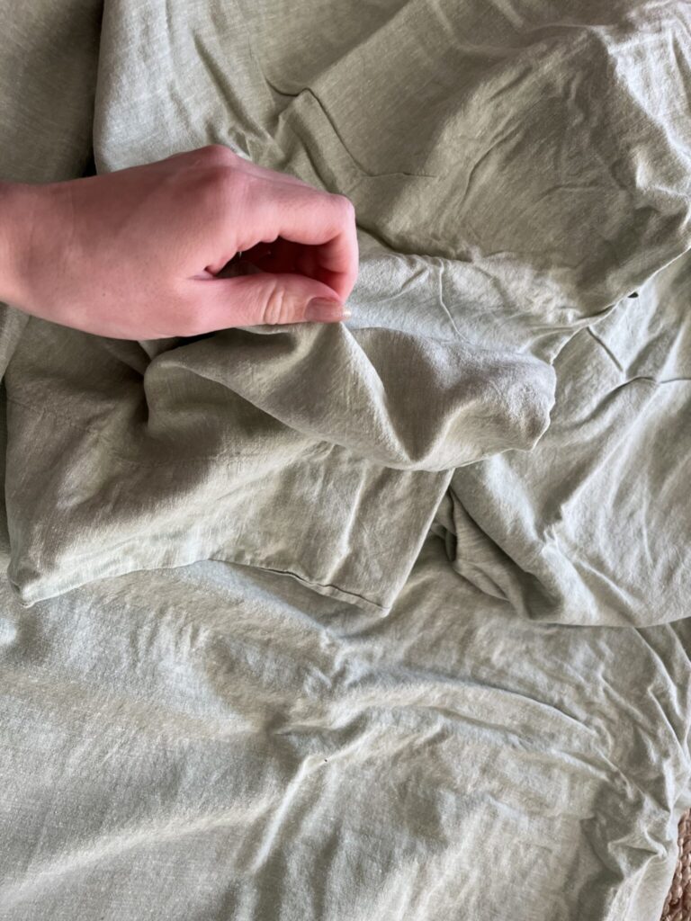A hand holds a corner of light green, wrinkled fabric spread out on a flat surface.