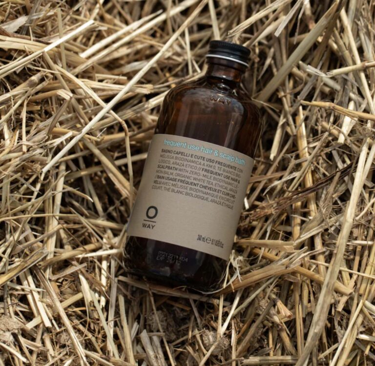 Amber glass Oway shampoo bottle labeled “Frequent Use Hair & Scalp Bath” on natural straw — sustainable shampoo packaging.