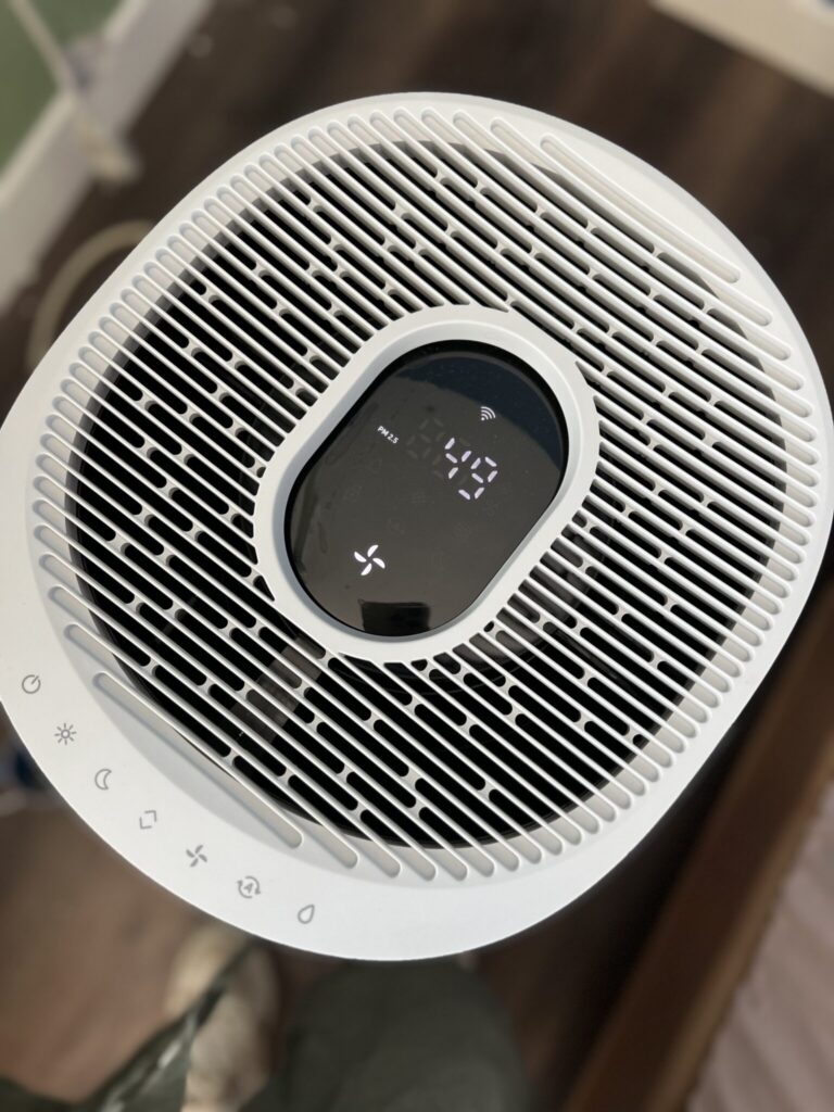 Top view of a white air purifier with digital display showing numbers and various touch control icons along the edge.
