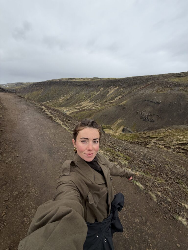 Qué significa realmente «alineación» y cómo utilizarla para hacer que tu vida fluya Person taking a selfie on a dirt path in a hilly, rocky landscape under an overcast sky.